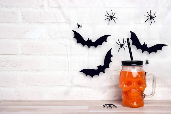 Orange Halloween cocktail in skull glass jars with cobwebs and bats. Copy space for text.