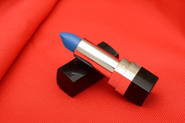 Lipstik warna biru pada latar belakang kain merah — Stok Foto