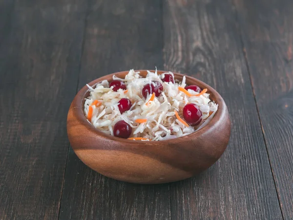 Traditional russian appetizer sauerkraut with cranberry and carrot in wooden bowl on brown rustic wooden table. Fermented cabbage. Russian cuisine and russian kitchen.