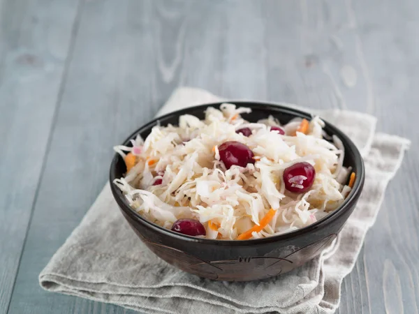 Traditional russian appetizer sauerkraut with cranberry and carrot in dark craft plate on gray rustic wooden table. Fermented cabbage. Russian cuisine and russian kitchen.