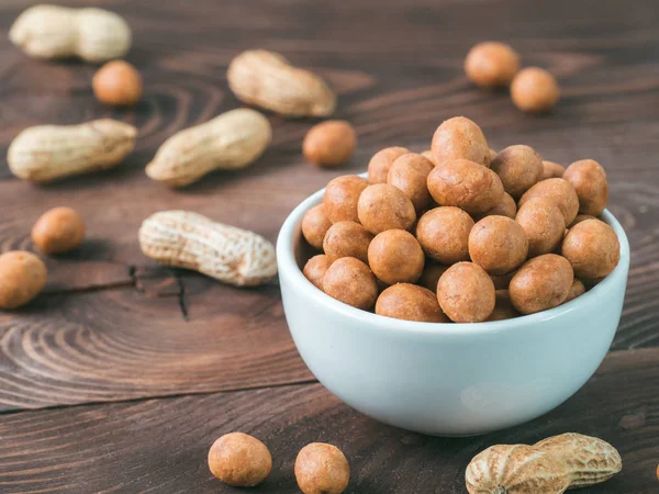 Peanut snack for beer, wine, party bar. Salted peanuts in coconut glaze on brown wooden table. Copy space.