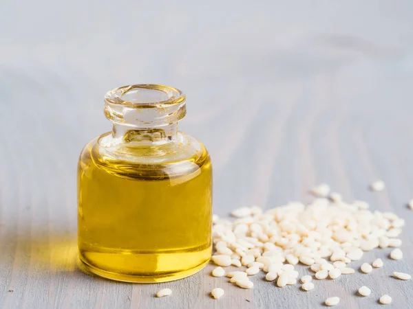 Bottle of sesame oil and sesame seeds on gray wooden table background. Copy space for text.