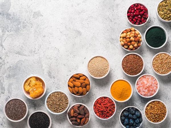 Various superfoods in smal bowl gray concrete background. Superfood as chia, spirulina, raw cocoa bean, goji, hemp, quinoa, bee pollen, black sesame, turmeric. Copy space for text. Top view, flat-lay.
