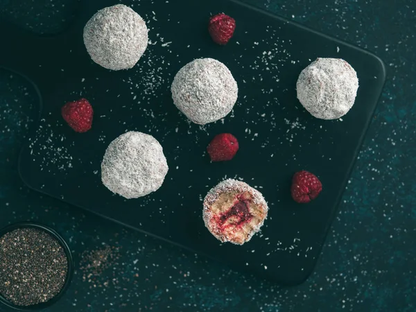 Raw vegan lamington bliss balls with raspberries chia jam on dark background. No baked healthy vegan sweet dessert idea and recipe. Top view or flat-lay.