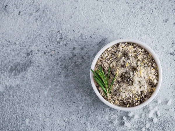 Sea salt scented herb rosemary and lemon zest. Sea salt with aromatic herbin small bowl on gray cement background. Scented salt and ingerdients. Copy space. Top view or flat lay