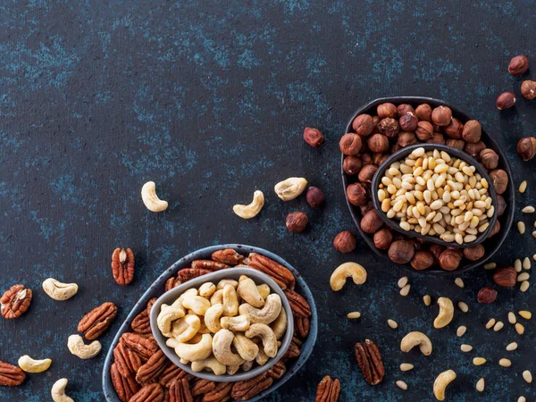 Background of nuts - cashew, pecan, pine nuts, hazelnuts - on dark blue background with copy space. Top view or flat lay