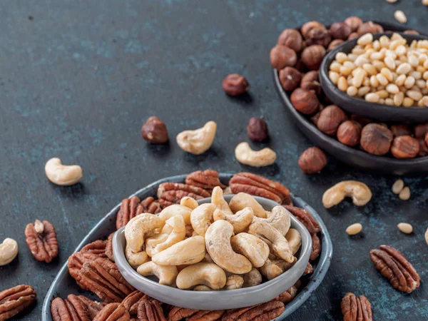 Background of nuts - cashew, pecan, pine nuts, hazelnuts - on dark blue background with copy space.