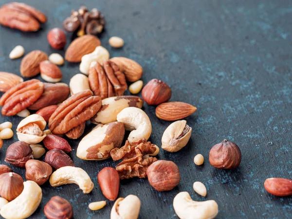 Background of nuts - cashew, pecan, pine nuts, hazelnuts - on dark blue background with copy space