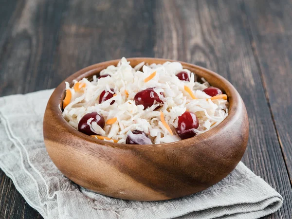 Traditional russian appetizer sauerkraut with cranberry and carrot in wooden bowl on brown rustic wooden table. Fermented cabbage. Russian cuisine and russian kitchen.