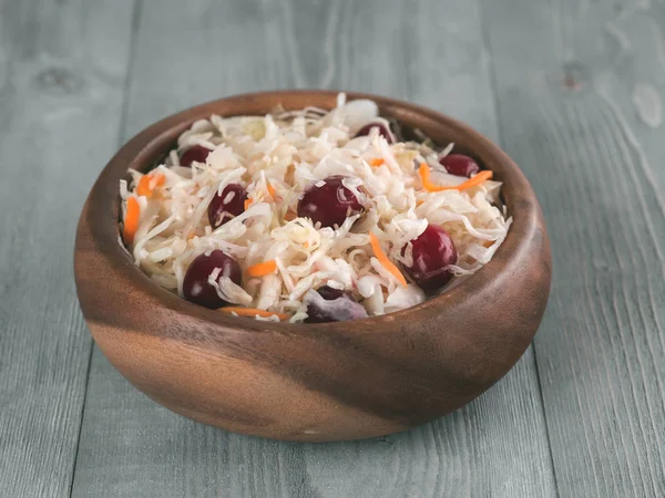 Traditional russian appetizer sauerkraut with cranberry and carrot in wooden bowl on gray rustic wooden table. Fermented cabbage. Russian cuisine and russian kitchen.