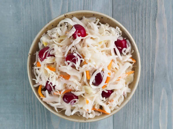 Traditional russian appetizer sauerkraut with cranberry and carrot in craft plate on gray rustic wooden table. Fermented cabbage. Russian cuisine and russian kitchen. Top view or flat-lay.