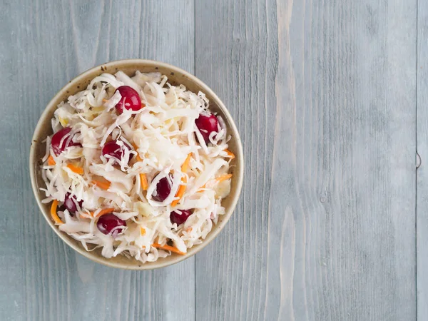 Traditional russian appetizer sauerkraut with cranberry and carrot in craft plate on gray rustic wooden table. Fermented cabbage. Russian cuisine and russian kitchen. Top view or flat-lay.