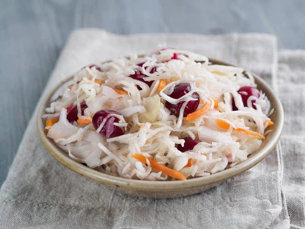 Traditional russian appetizer sauerkraut with cranberry and carrot in craft plate on gray rustic wooden table. Fermented cabbage. Russian cuisine and russian kitchen.