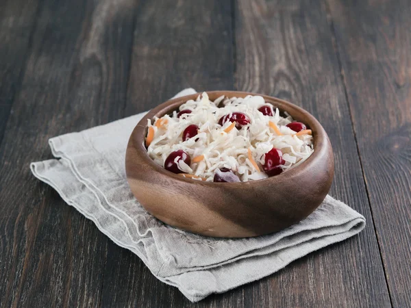 Traditional russian appetizer sauerkraut with cranberry and carrot in wooden bowl on brown rustic wooden table. Fermented cabbage. Russian cuisine and russian kitchen.