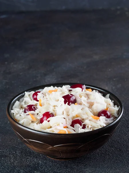 Traditional russian appetizer sauerkraut with cranberry and carrot in dark bowl on black cement background. Fermented cabbage. Russian cuisine and russian kitchen. Copy space.