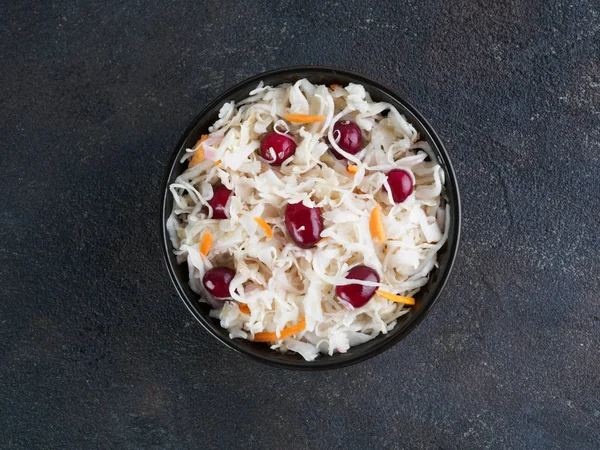 Traditional russian appetizer sauerkraut with cranberry and carrot in dark bowl on black cement background. Fermented cabbage. Russian cuisine and russian kitchen. Top view or flat-lay. Copy space.