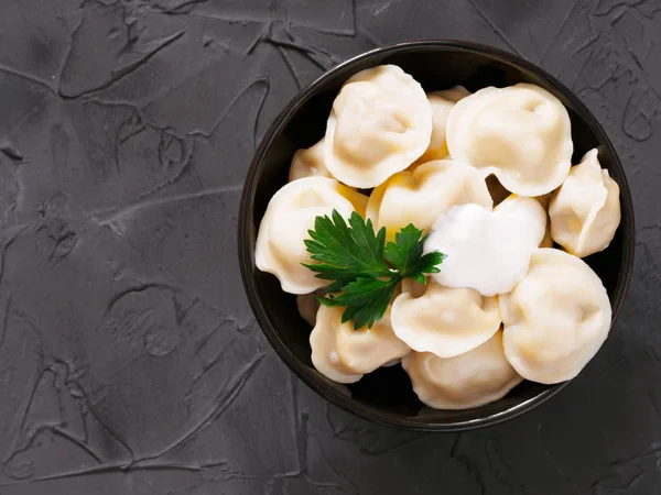 Traditional russian pelmeni, ravioli, dumplings with meat on black concrete background. Copyspace. Top view or flat lay. Russian food and russian kitchen concept.