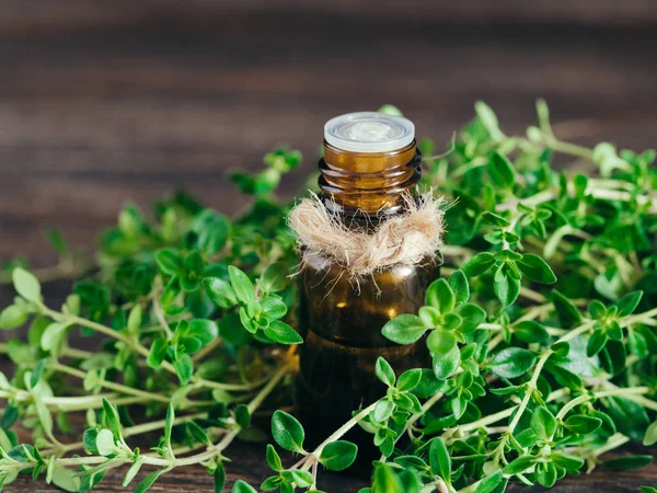 thyme essential oil in dark glass bottle and fresh thyme on dark brown wooden background with copy space