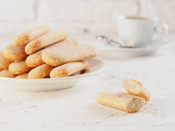 Italian cookie savoiardi and cup of coffee. Close up view of ladyfinger biscuit cookie on white concrete background. Copy space.