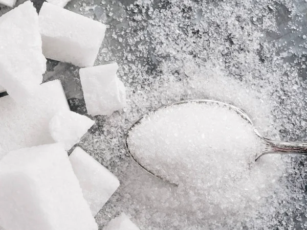 Sugar background. Sugar cubes and granulated sugar in spoon. White sugar on gray galvanized iron background. Top view or flat lay. Copy space.