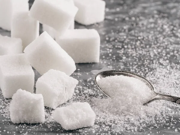 Sugar background. Sugar cubes and granulated sugar in spoon. White sugar on gray galvanized iron background. Copy space.