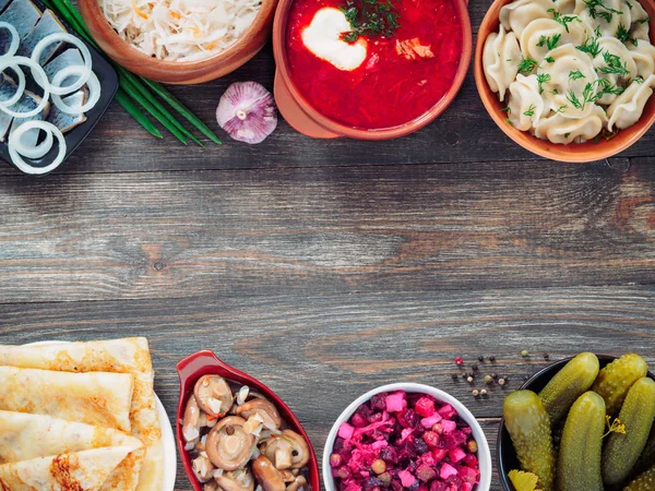 Russian food on wooden background. Assortment dishes of Russian cuisine - borscht, pelmeni, herring, marinated mushrooms, salted cucumbers, vinaigrette, sauerkraut and pancakes. Top view. Copy space. — Stock Image Russian Food Wooden Background Assortment Dishes Russian Cuisine Borscht Pelmeni Royalty Free Stock Images