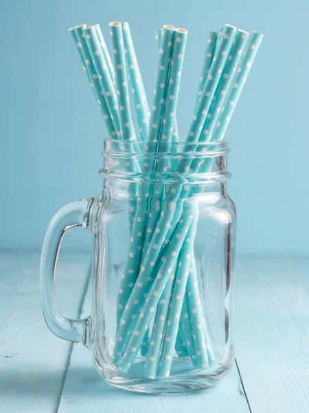 Mason jars with blue paper straws on blue wooden background. Ideal for summer drinks and smoothies. Vertical