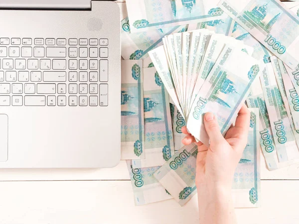 Hand holding russian rubles near laptop on table with banknotes. Top view or flat lay. Finance and earning concept