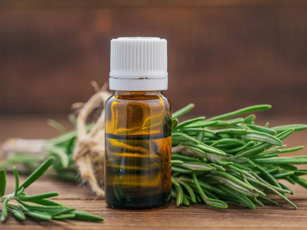 Rosemary essential oil in dark glass bottle and fresh rosemary on dark wooden background with copy space