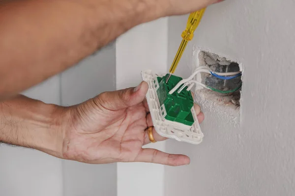 Elektrikçi güç kablosunu duvardaki kontrol etmek için bir tornavida kullanarak.