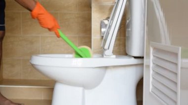 Turuncu lastik eldiven giyen bir adamın elini bir tuvalete parlatma dönüştürmek için kullanılır.