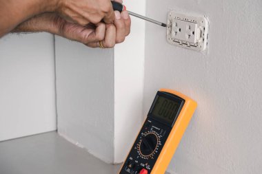 Elektrikçi güç kablosunu duvardaki prize takmak için bir tornavida kullanarak.