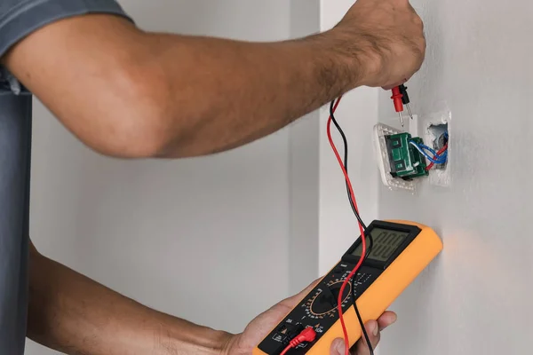 Elektrikçi duvardaki prize gerilim ölçmek için bir dijital metre kullanıyor.