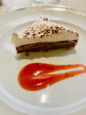 Çürük çikolata ve kremalı tatlı beyaz bir tabakta servis edilir, çikolata tabanı, kremalı orta tabaka, ve çikolata parçacıkları serpiştirilmiş çırpılmış