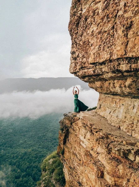 Dağlarda kenarında duran uzun yeşil elbise giyen genç kadın