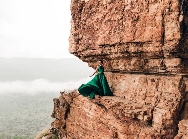 Dağlarda kenarında duran uzun yeşil elbise giyen genç kadın