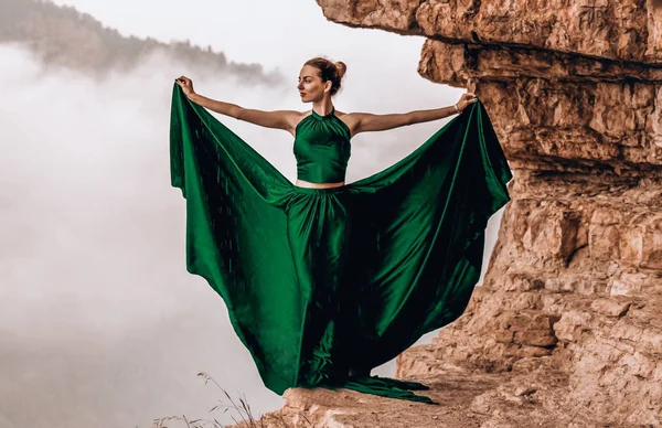 Dağlarda kenarında duran uzun yeşil elbise giyen genç kadın