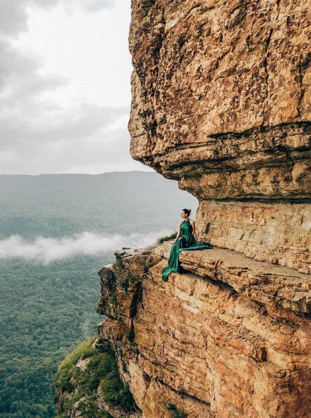 Dağlarda kenarında oturan uzun yeşil elbise giyen genç kadın