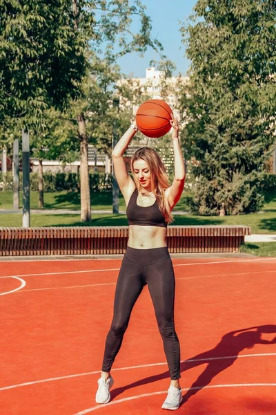 Formda vücutlu genç kadın basketbol oynuyor ve sahada eğleniyor. Güneşli bir gün.