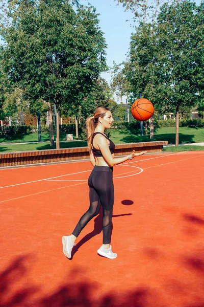 Young woman with fit body playing basketball and having fun on court. Sunny day.