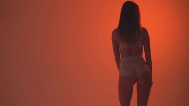 Kız dans turuncu bir arka plan üzerinde beyaz iç çamaşırı. Ağır çekim 60fps