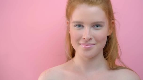 Nahaufnahme einer geheimnisvollen Ingwerfrau, die auf rosa Hintergrund in die Kamera blickt — Stockvideo