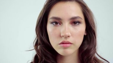 Genç kadın beyaz arka planda gözlerini aç. Stüdyoda kameraya bakan gülümseyen kıza yaklaş. Kadın doğası güzelliği