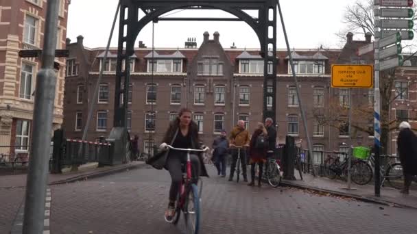 Amsterdam, Holandia, listopad 2019. Ludzie jeżdżący na rowerze i spacerujący po moście przez kanał w Amsterdamie. — Wideo stockowe