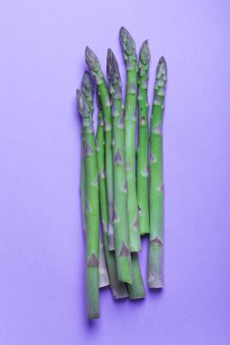 Banches of fresh green asparagus on purple background. Vertical clipart