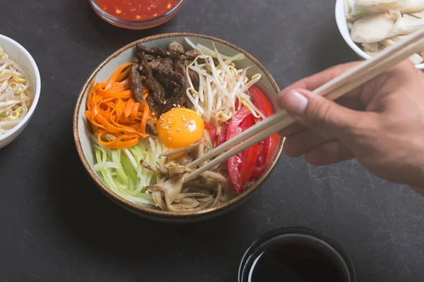 쌀과 어두운 배경에서 야채와 함께 전통적인 아시아 비빔밥 요리. 남자는 젓가락을 사용 하 여 요리 — 스톡 사진