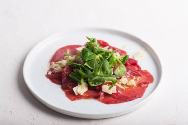 Dana carpaccio roka salatası, parmesan ve beyaz tabakta sos ile