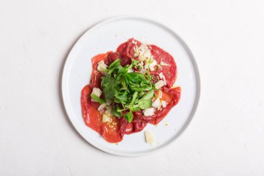 Dana carpaccio roka salatası, parmesan ve beyaz tabakta sos ile