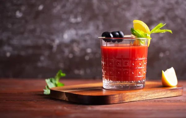 Cóctel Bloody Mary con hielo, sal y aperitivos en vaso sobre una mesa de madera con espacio para copiar. Estilo de imagen oscura — Foto de Stock