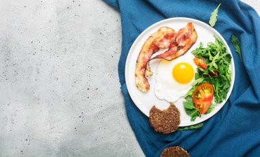 Tabak üzerinde yumurta, kızarmış domuz pastırması ve roka ile doyurucu yüksek protein İngiliz tarzı kahvaltı. Üstteki görünüm, yatay oryantasyon